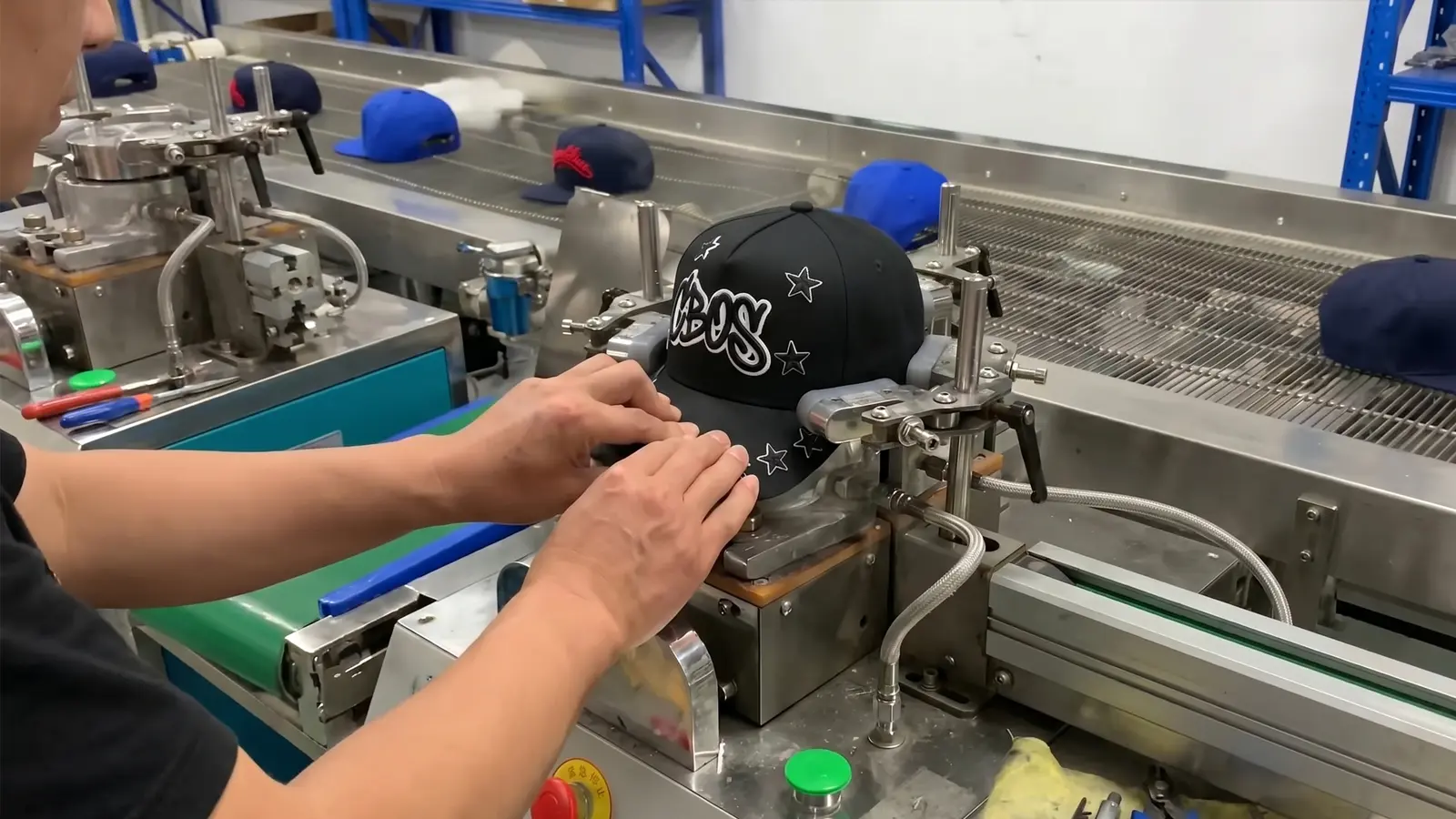 Black CBOs cap clamped on an embroidery machine while a run of navy caps moves down the production line